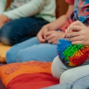 Kinder sitzen mit mit Kissen beim Philosophieren auf dem Boden, ein Kind hat den Gesprächsball "Wuschel" in der Hand, das Bild zeigt einen Ausschnitt und so sieht man tatsächlich nur die Unterkörper von drei Kindern