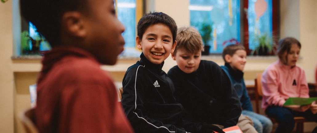 Ein junge sitzt im Stuhlkreis und lacht.