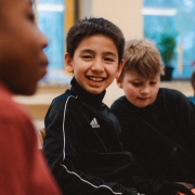 Ein junge sitzt im Stuhlkreis und lacht.