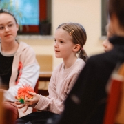 Ein junges Mädchen sitzt in einem Stuhlkreis und hält einen Gesprächswuschel in der Hand.
