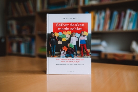 Das Buch "Selber denken macht schlau" steht vor einem Bücherregal.
